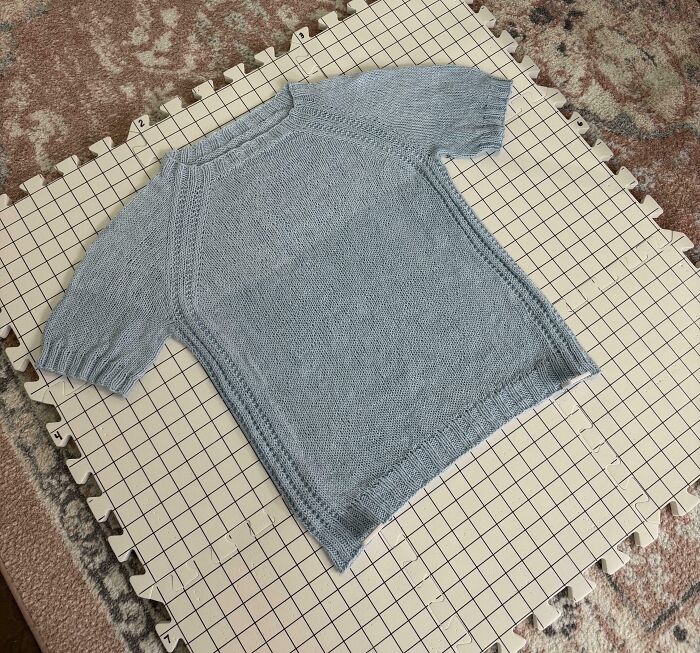 Light blue knitted shirt drying on a gridded foam board, showing a funny way people learned their lesson in knitting.