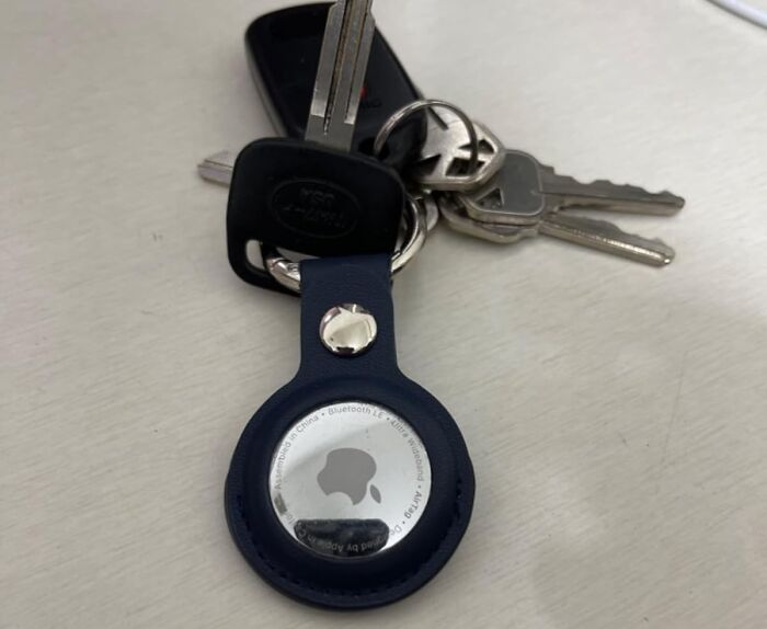 Durable keychain with an Apple AirTag attached to multiple metal keys on a white surface.