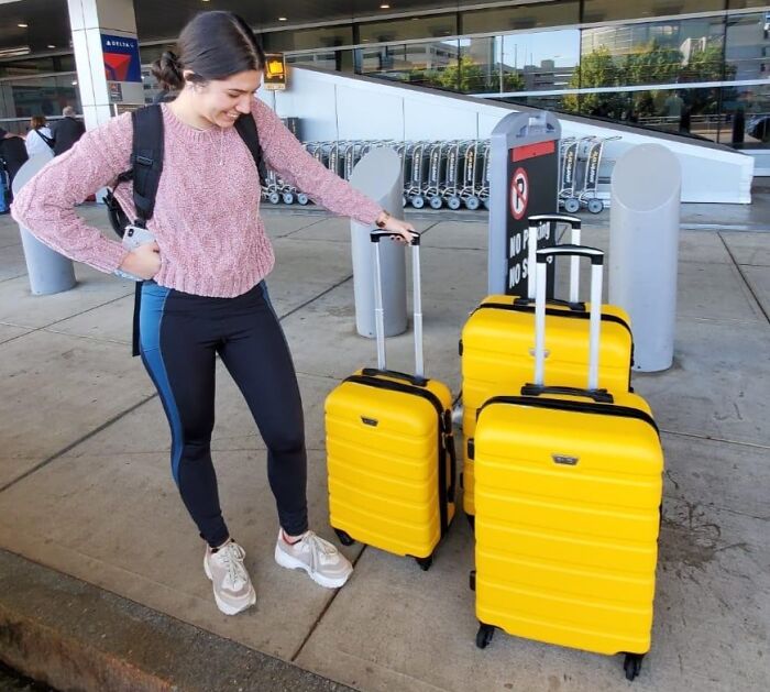 Woman at airport with durable bright yellow suitcases, showcasing travel gear built to last and withstand rough handling.