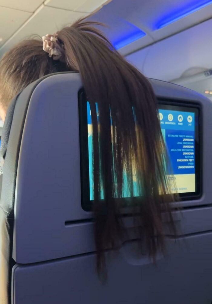 Passenger with long hair draped over an airplane screen showing no care about rules and etiquette on a flight.