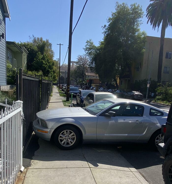 Silver car parked blocking a sidewalk, showing blatant disregard for rules and etiquette in an urban neighborhood.