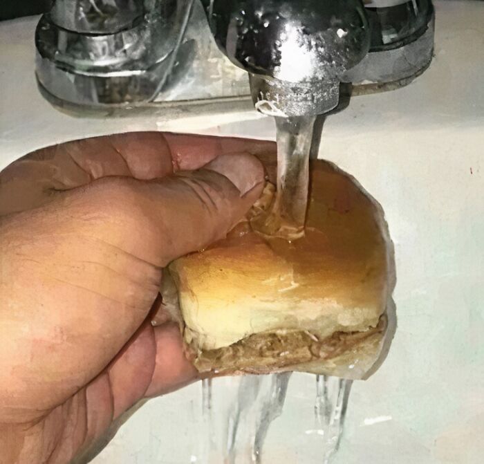 Hand holding a sandwich under running faucet water, highlighting food nobody should eat for health concerns.