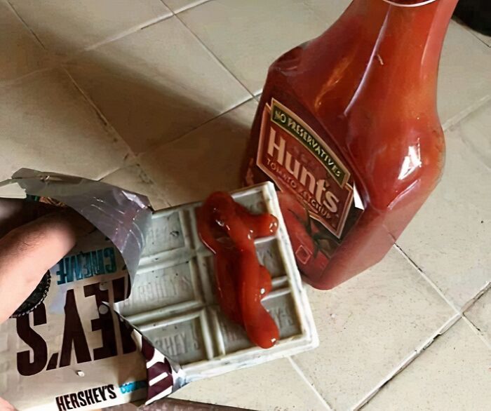 Hershey’s white chocolate bar with ketchup sauce on top next to a bottle of Hunt’s ketchup on a tiled surface.