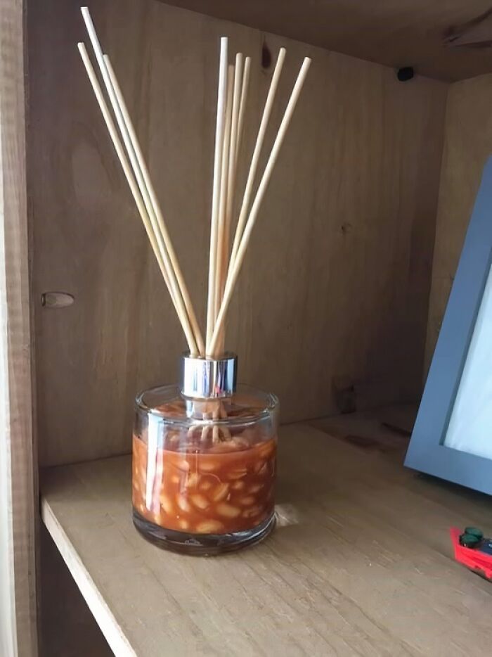 Glass container filled with baked beans used as a diffuser with wooden sticks on a wooden shelf, unhealthy food concept.