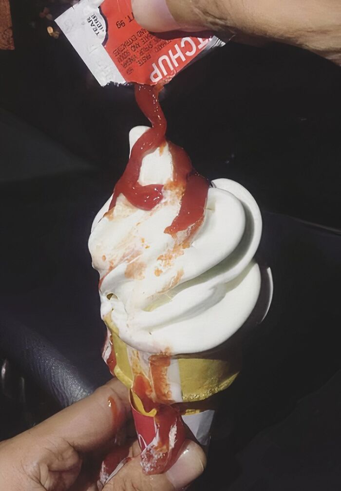 Soft serve ice cream cone being topped with ketchup, illustrating unhealthy food choices and poor mental health impact.