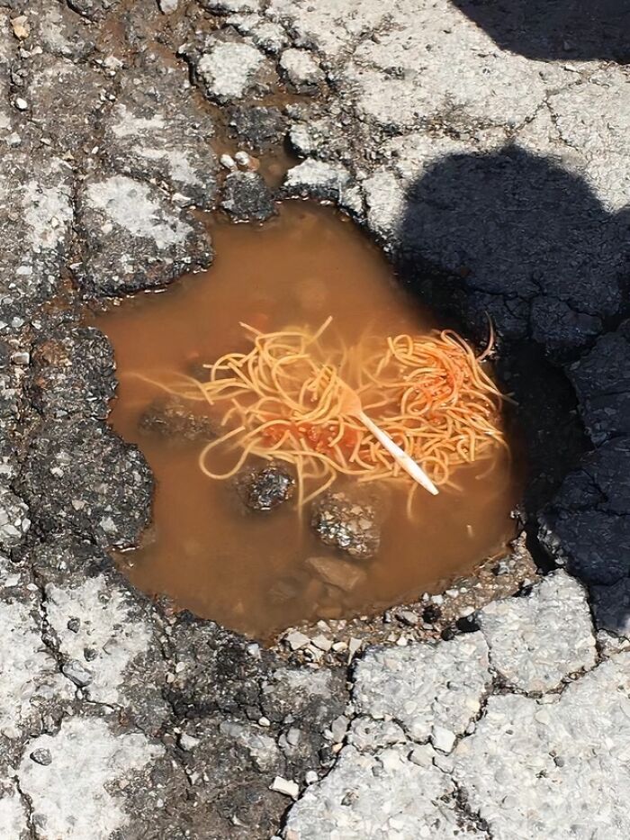 Spaghetti discarded in a dirty pothole filled with murky water, illustrating unhealthy food waste and poor physical health risks.