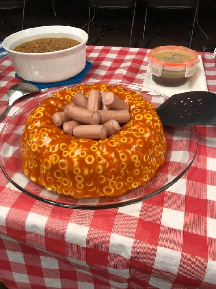 Spaghetti-o jello mold topped with sliced hot dogs on a red and white checkered tablecloth, unusual food combination.