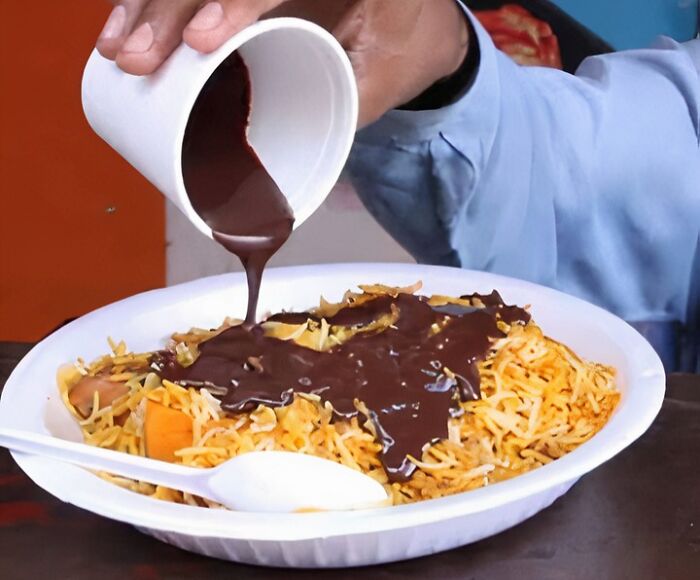 Person pouring thick chocolate sauce over a plate of noodles, illustrating food nobody should eat for health.