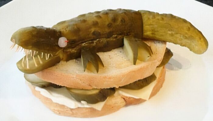 Pickle crafted into a small crocodile shape placed on a sandwich illustrating unusual food nobody should eat.