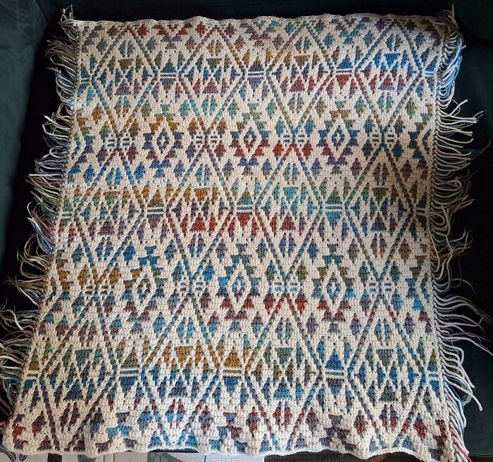 Crocheted blanket with colorful geometric patterns and fringed edges showcasing mastery in crocheting projects.