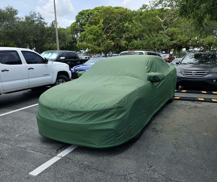 Car covered with a green cover parked improperly over two parking spaces, showing disregard for rules and etiquette.