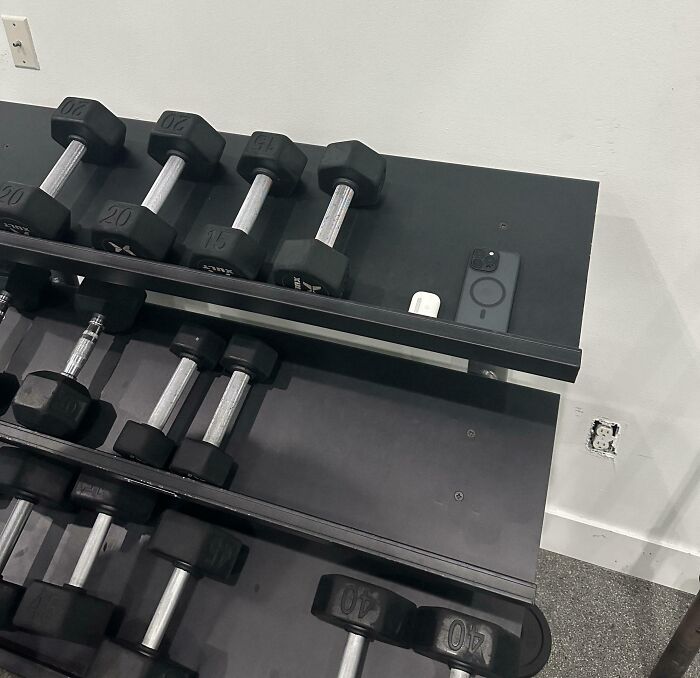Gym dumbbells arranged with a phone and AirPods placed improperly, showing a lack of care about rules and etiquette.