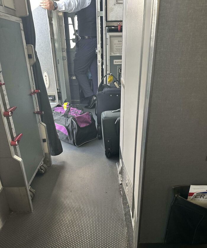 Luggage blocking airplane aisle with a crew member standing nearby, showing disregard for rules and etiquette.