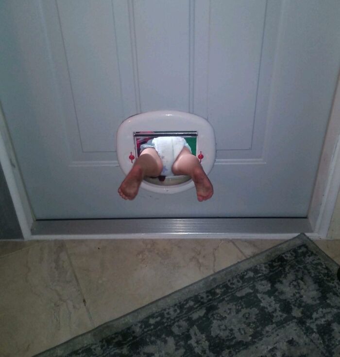 Toddler stuck halfway through cat door in a white diaper, showcasing funny ways people learned their lesson at home.