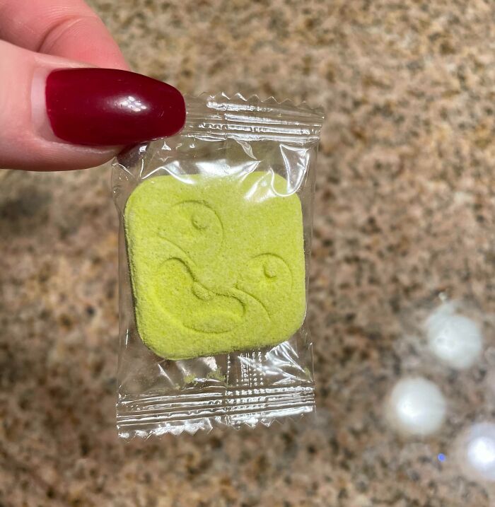 Hand holding a small yellow square candy with a funny face in clear plastic, illustrating funny ways people learned their lesson.