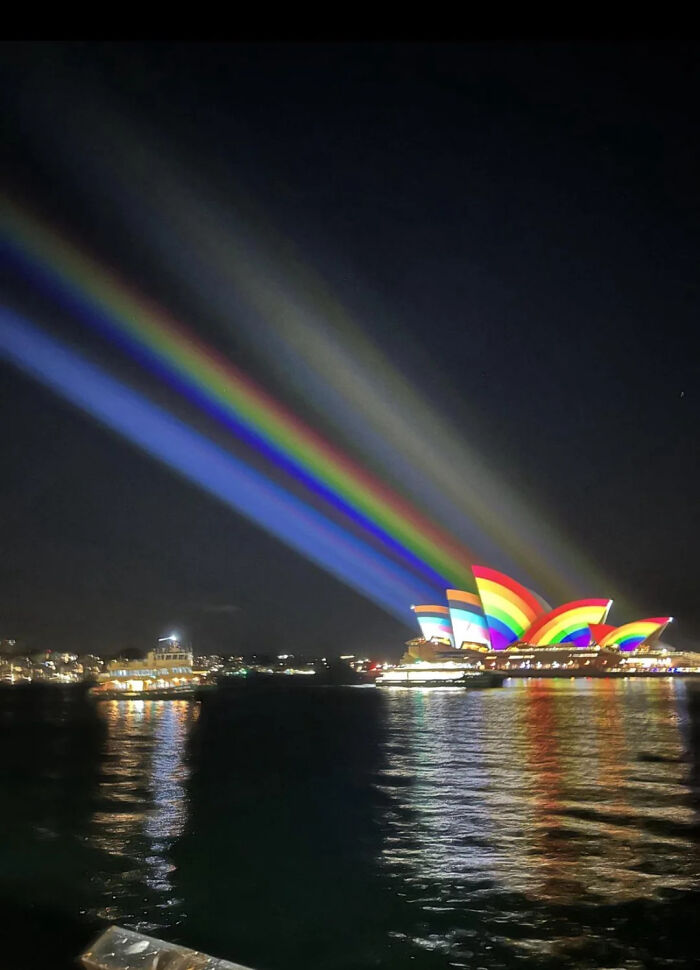 Sydney Opera House lit up with rainbow projections at night, symbolizing chaotic good and unique acts of kindness.