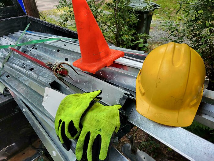 Yellow construction helmet, work gloves, safety cone, and metal scraps found as dumpster diving treasures outdoors.