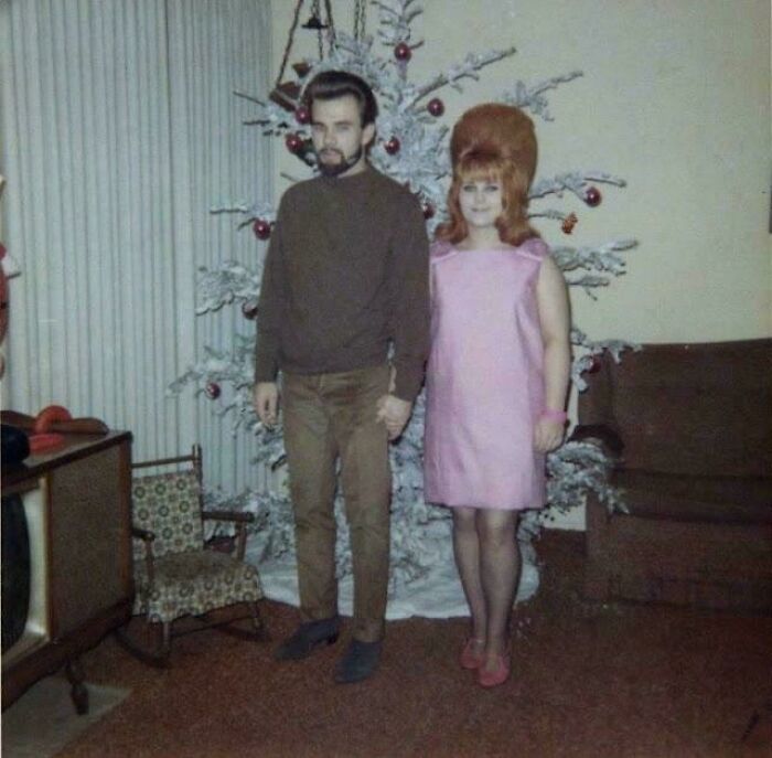 Couple in vintage clothing standing by a decorated Christmas tree, offering candid glimpses into the past.