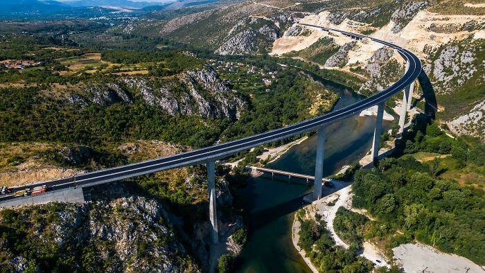 Curved elevated highway bridge over river and valley, showcasing brilliant infrastructure in a mountainous landscape.
