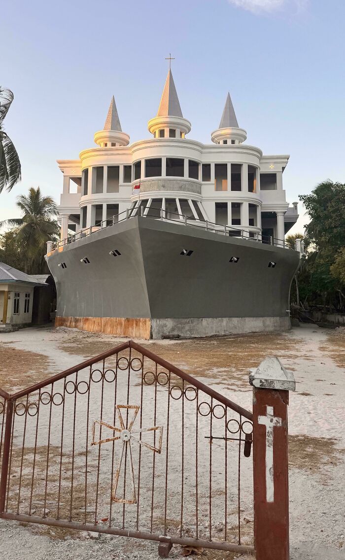 Bizarre building designed like a large ship with pointed towers, set behind a rusty iron gate with a cross design.