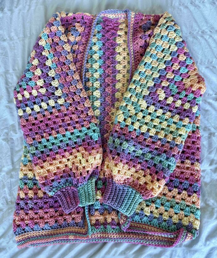 Crocheted multicolored granny square sweater with pastel hues, showcasing expert crocheting skills and intricate stitch work.