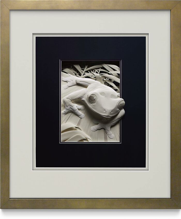 Paper wildlife sculpture of a frog with detailed leaves, showcasing realistic texture and depth in a framed artwork.