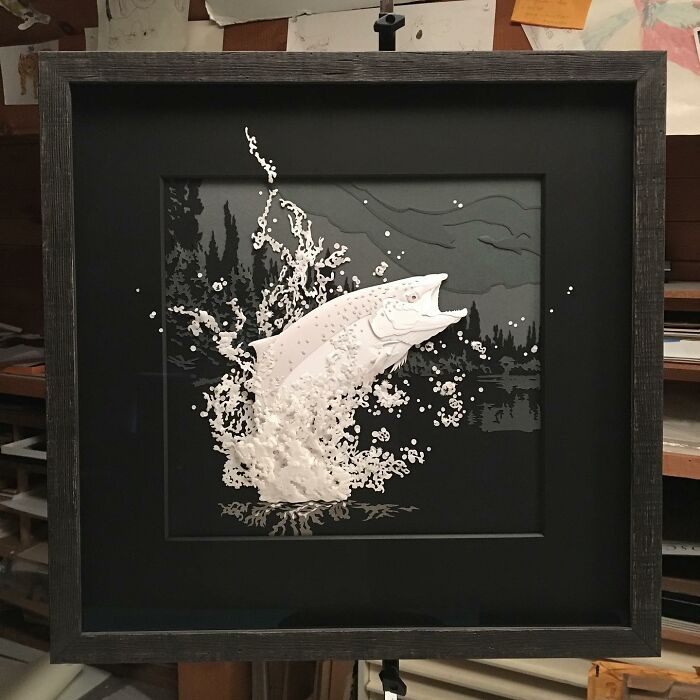 Realistic wildlife sculpture of a fish leaping from water, made from layered and textured simple paper artwork in a black frame.