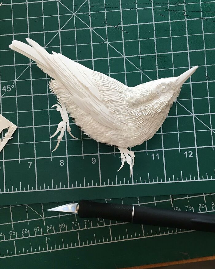 Intricately detailed wildlife sculpture of a bird carved from simple white paper, showcasing realistic feather textures.