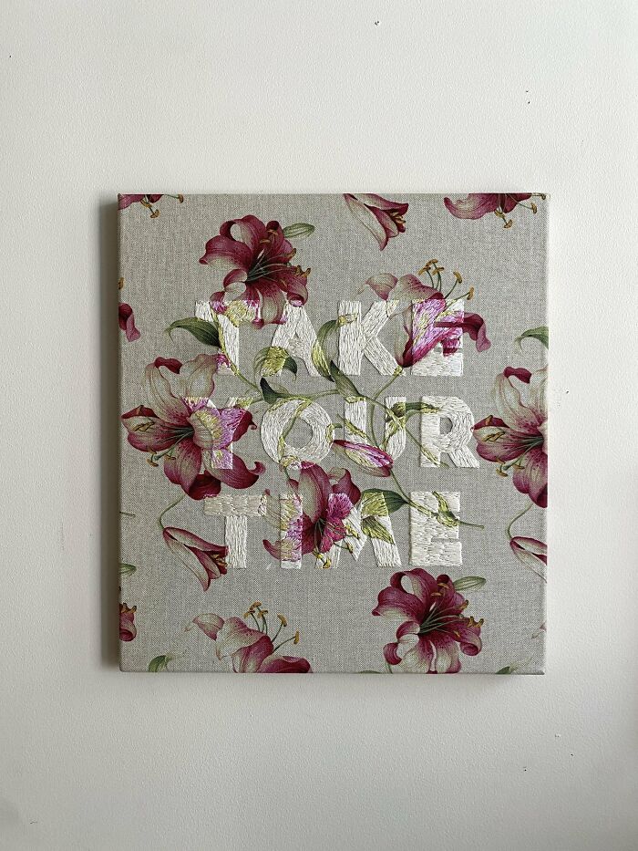 Floral fabric canvas embroidered with white and colored thread forming the words take our time, showcasing embroidery skills.