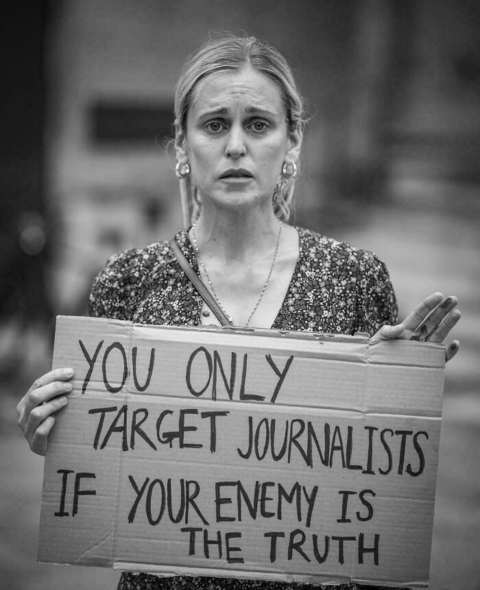Woman holding a cardboard sign protesting targeting journalists, capturing the essence of boring dystopia in modern life.
