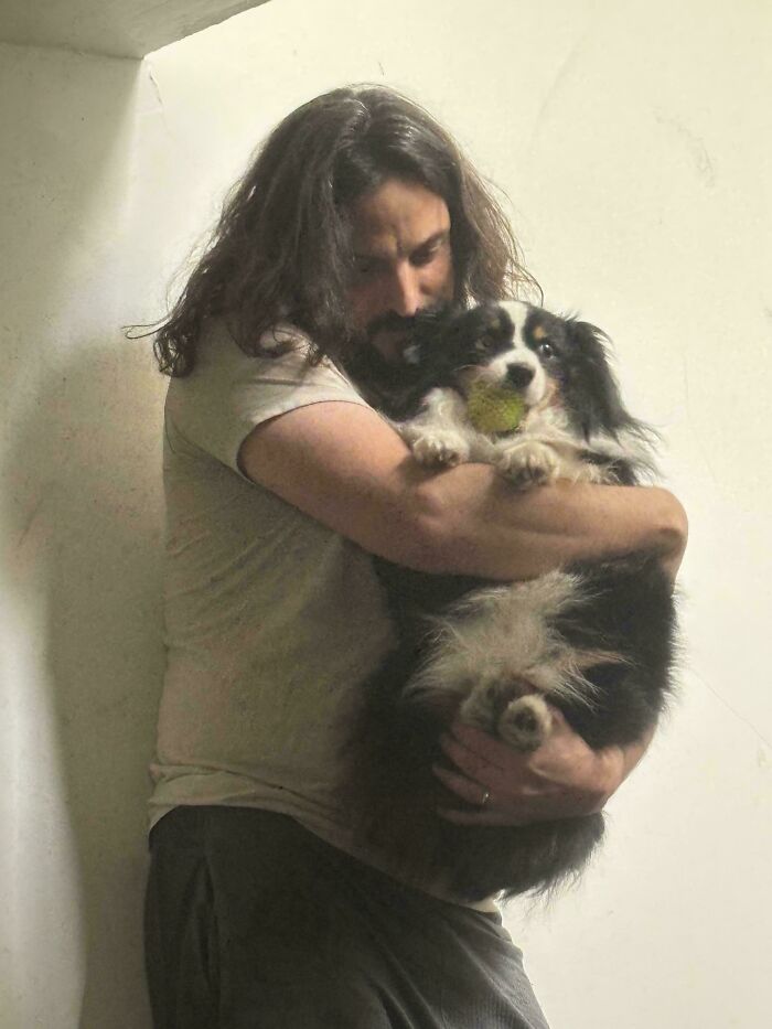 Man embracing a dog holding a tennis ball in its mouth, captured in a soft light for accidental renaissance photos.