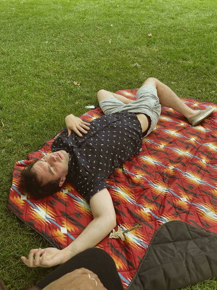 Man lying on a patterned blanket on grass, captured in an accidental renaissance style photo with natural lighting.