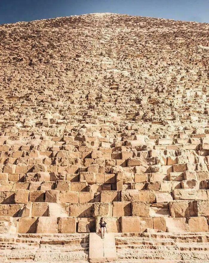 A tiny figure sits at the base of the incredibly large, massive stone blocks of an ancient pyramid, highlighting how extremely large things can be scary.
