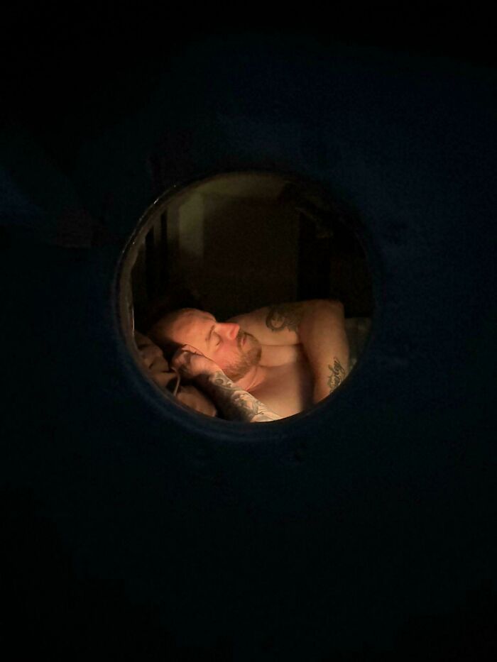 Man with tattoos sleeping peacefully viewed through a round window, creating an accidental Renaissance photo effect.