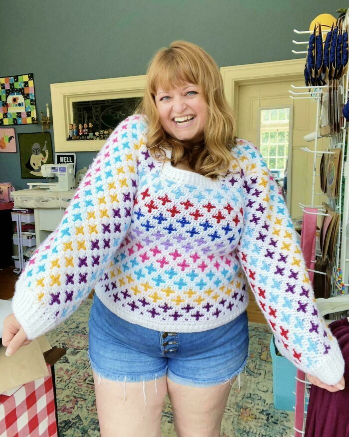 Woman in a colorful crocheted sweater smiling indoors, showcasing the art of crocheting in a cozy creative space.
