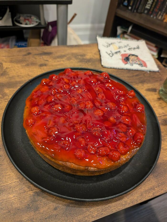 Cherry-topped baked goods on a black plate showcasing the glossy, vibrant fruit topping on a rustic wooden table.