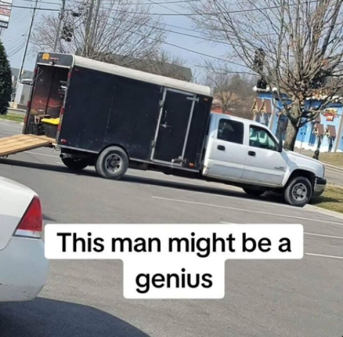 Pickup truck with a trailer using a wooden ramp in a clever redneck engineer creation in a parking lot.