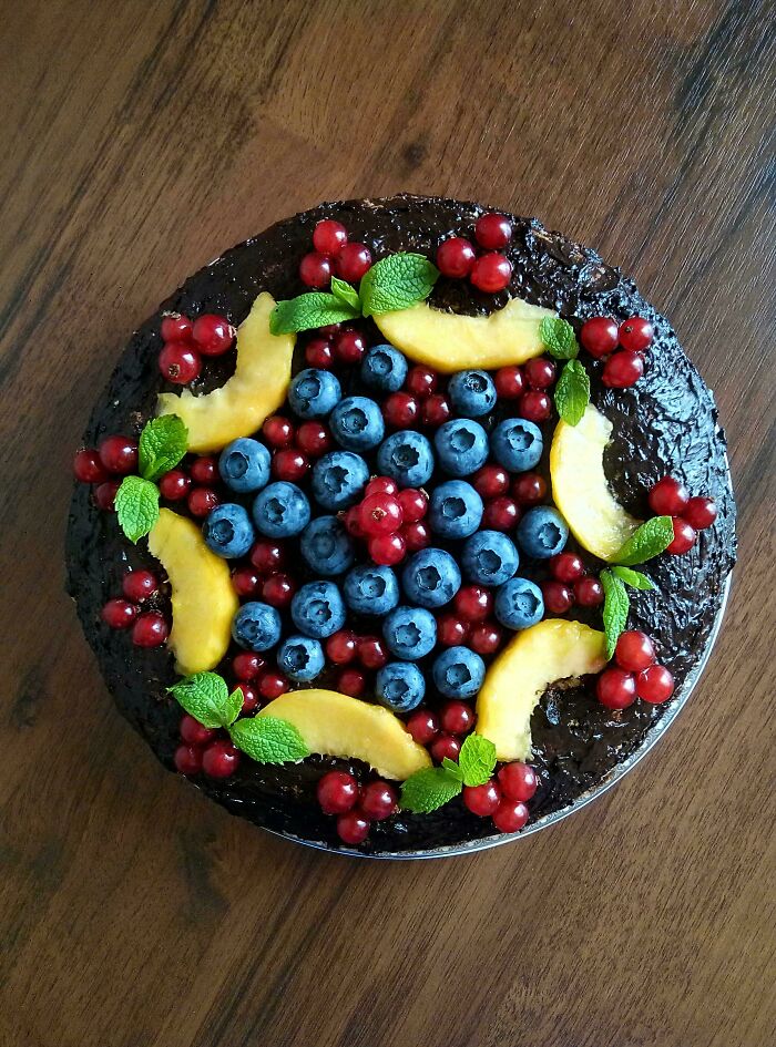 Chocolate baked good topped with blueberries, red currants, peach slices, and fresh mint leaves on a wooden table.