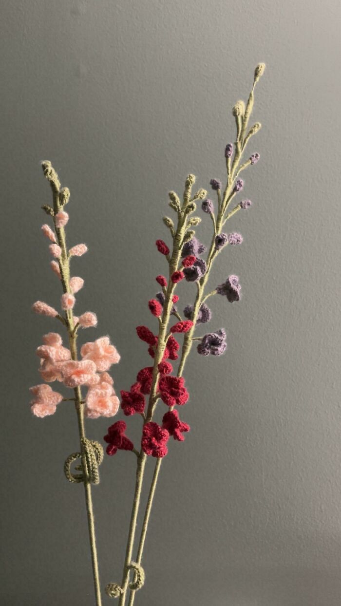 Delicate crocheted flower stems in pink, red, and purple shades displayed against a neutral background.