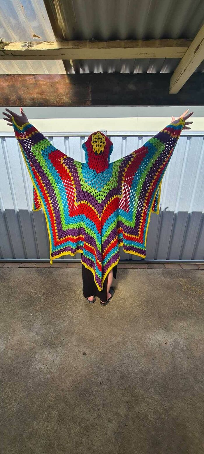 Person wearing a colorful, striped crocheted shawl with arms raised, showcasing a mastered crocheting project.