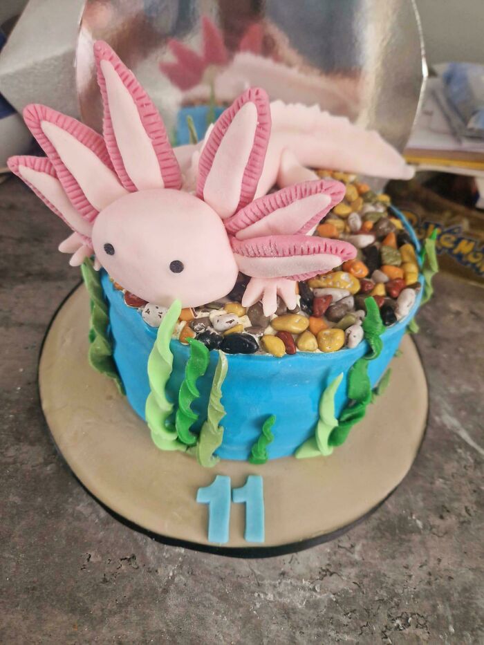 Decorated blue baked goods cake with edible sea plants and a pink axolotl figure on top for an 11th birthday.