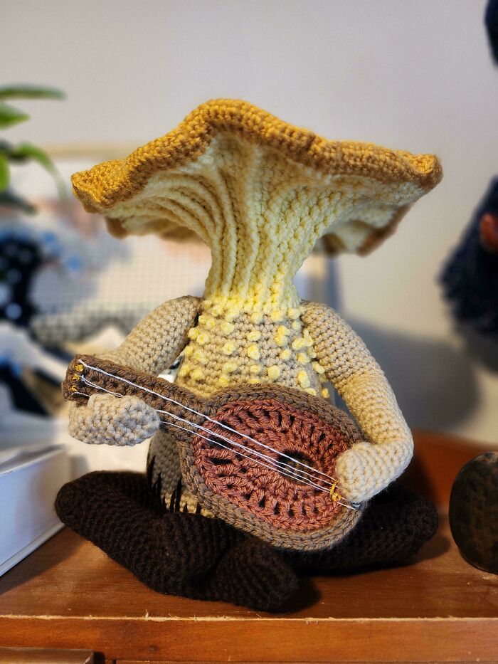 Crocheted figure resembling a mushroom playing a stringed instrument, showcasing creative crocheting craftsmanship.