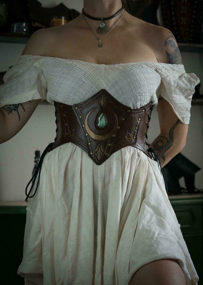Handcrafted leather corset belt with intricate designs worn over off-shoulder white dress, showcasing something people made cool.