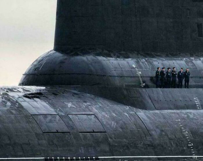A close-up of an extremely large submarine with a crew standing on its deck, highlighting its scary and eerie size.