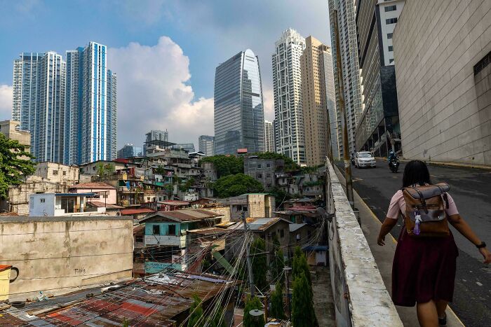 A person walking near rundown homes contrasted with towering modern skyscrapers in a $58 billion ghost city.