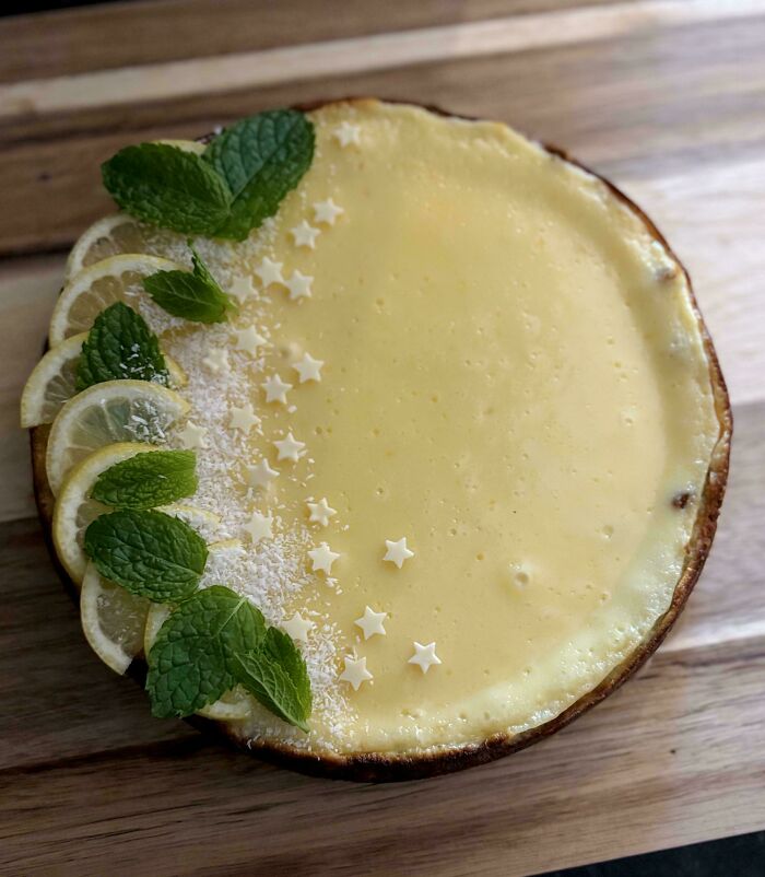 Lemon tart garnished with fresh mint, lemon slices, and white star-shaped sprinkles on a wooden surface.