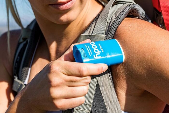 Woman applying deodorant while wearing a backpack, highlighting convenience of self-checkout aisle and discreet packaging.