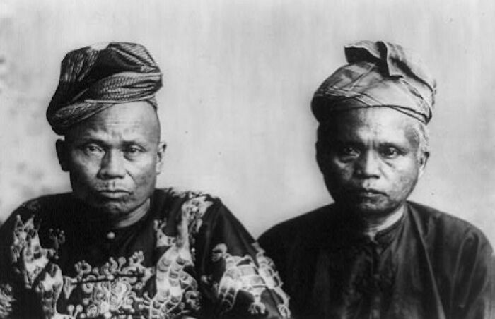 Two Filipino men from the 1890s wearing traditional clothing and headgear, showcasing cultural contrasts in the Philippines.