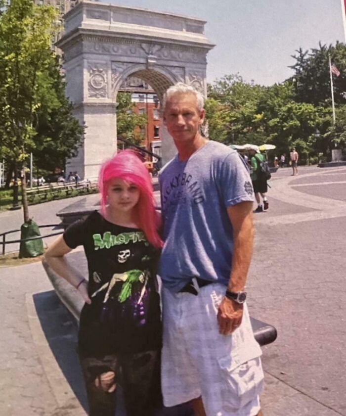 Teen with bright pink hair and a man posing in front of a city arch, part of regrettable past pics collection.