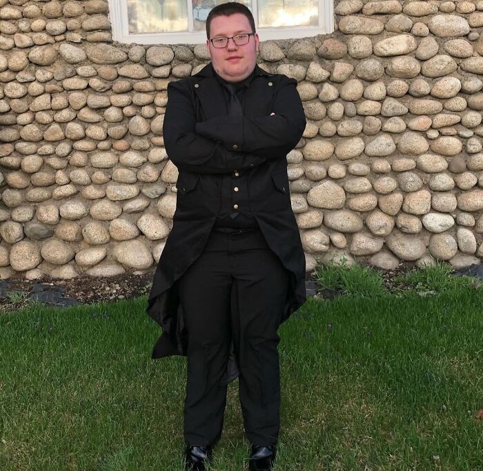 Person in black outfit posing with arms crossed in front of a stone wall, a cringeworthy regrettable past fashion moment.